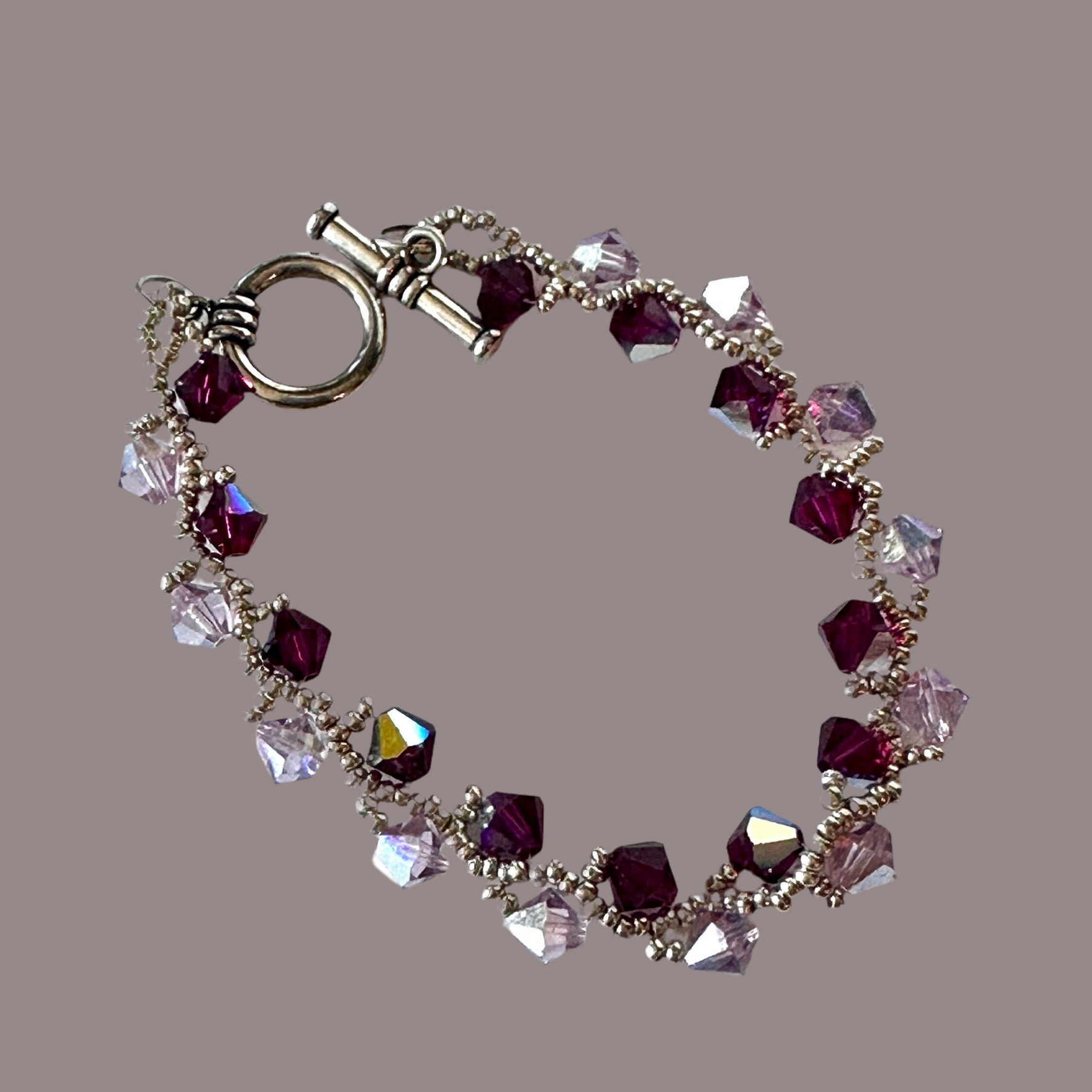 Ruby and light amethyst Swarovski Crystals, hand-woven with silver Miyuki seed beads, and finished with a toggle clasp.