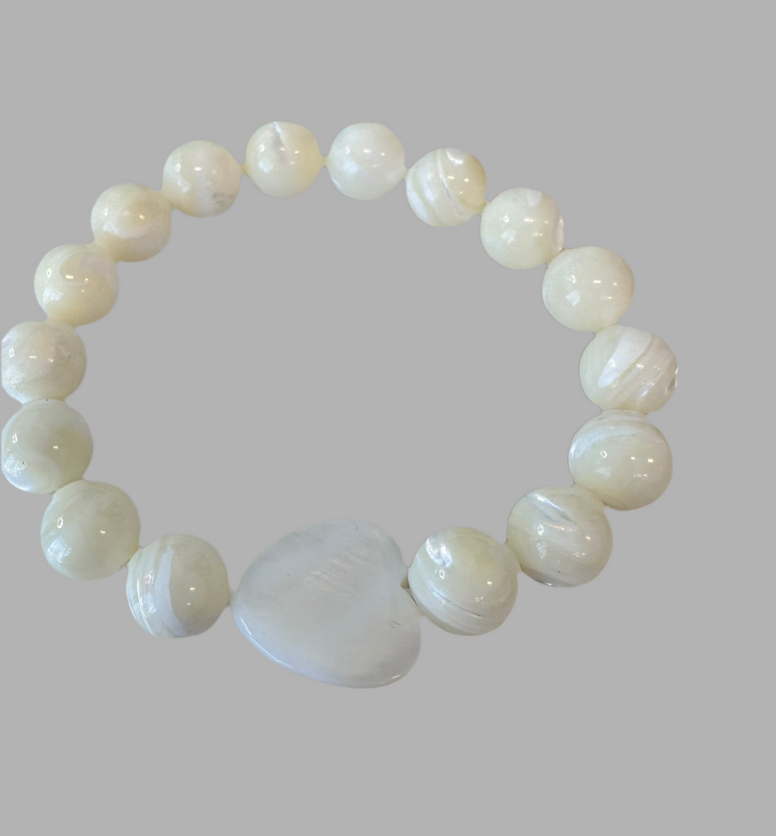 This Mother of Pearl Stretch Bracelet is expertly handmade and features a seashell heart spacer. Ideal for a special gift-giving occasion.