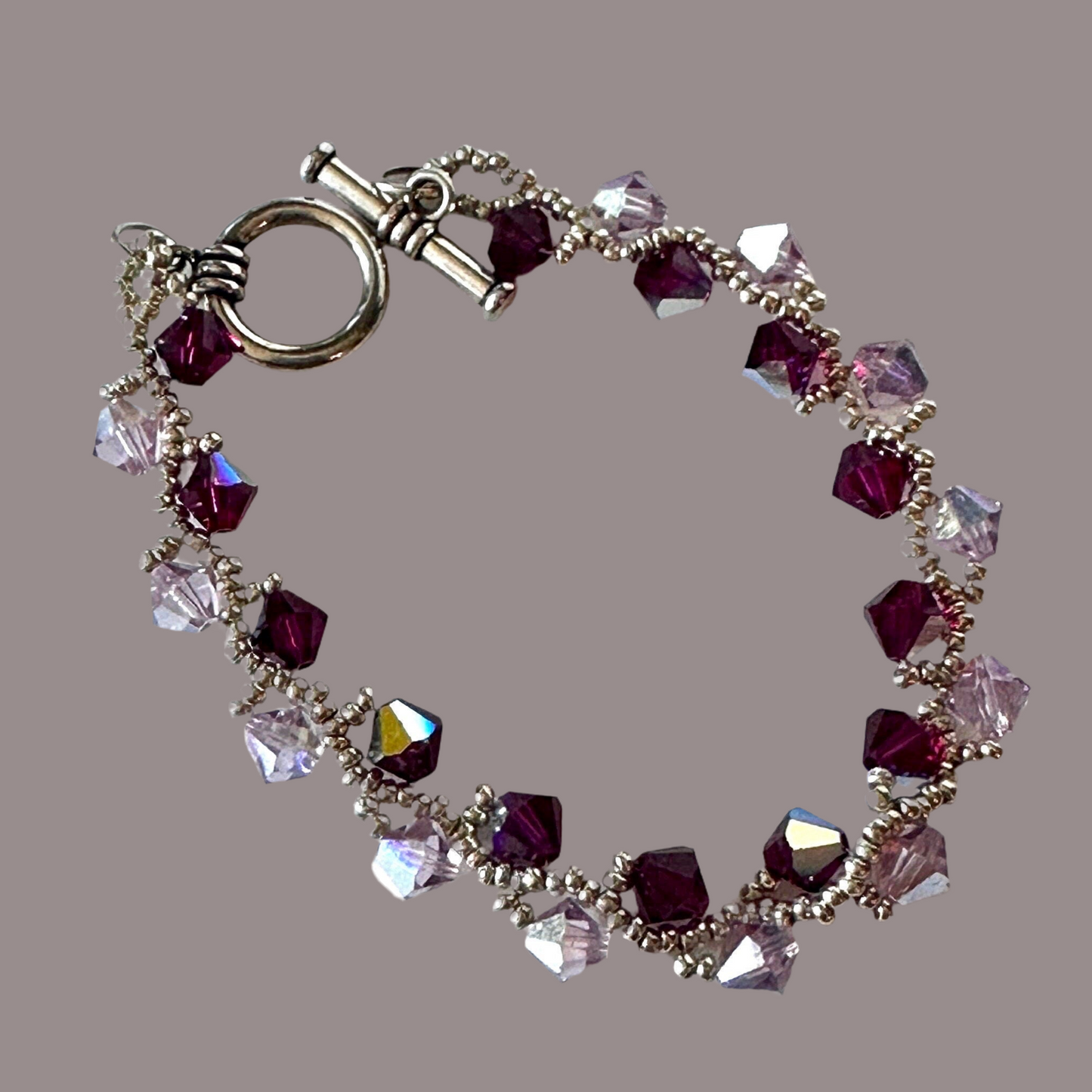 Ruby and light amethyst Swarovski Crystals, hand-woven with silver Miyuki seed beads, and finished with a toggle clasp. - Creations by Rosa