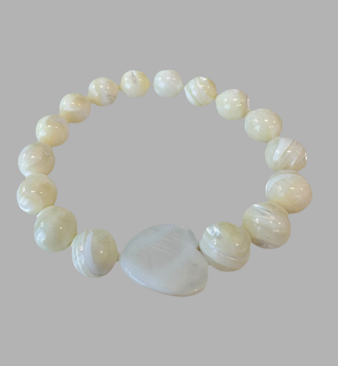 This Mother of Pearl Stretch Bracelet is expertly handmade and features a seashell heart spacer. Ideal for a special gift-giving occasion.